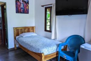 ein kleines Schlafzimmer mit einem Bett und einem blauen Stuhl in der Unterkunft Didi Lodge - Cabaña cálida y acogedora! in Cañas