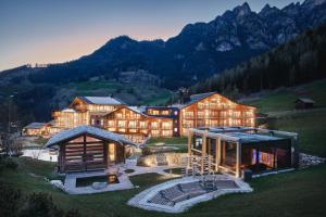 a large house on a hill with mountains in the background at Cyprianerhof Dolomit Resort in Tires