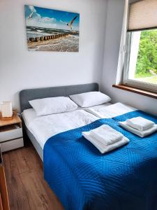 a bedroom with a bed with a blue blanket and a window at Apartament HARPUN nad morzem in Rusinowo