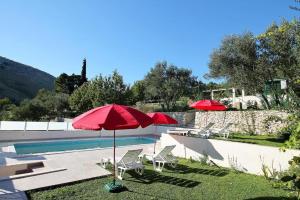 a swimming pool with two red umbrellas and two chairs and a swimming pool at Villa Marietta Equino in Donje Sitno