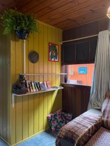 a room with a yellow wall and a shelf with books at Hostel Antônio Pescador Guarda do Embau in Guarda do Embaú