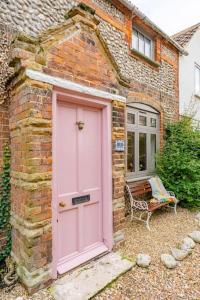 een roze deur van een bakstenen huis met een bank bij The Doll's House in Holt