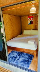 Cama en habitación pequeña con alfombra azul en โฮมสเตย์ เนเจอร์ เดอ สะปัน en Ban Huai Ti