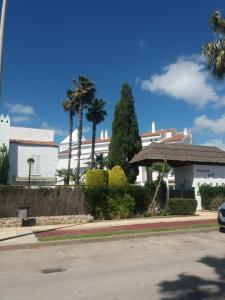 a white building with palm trees on a street at La Casita de Marina Golf-Costa Ballena in Cádiz
