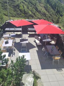 Täschalp Restaurant&Lodge في تاش: فناء به طاولات ومظلات وكراسي حمراء