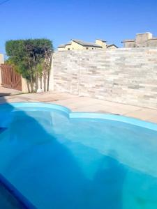 a blue swimming pool in front of a stone wall at Casa Rústica em Morro Branco - na quadra da praia in #N/A
