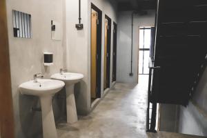 a bathroom with two white sinks and a hallway at The Cube Hostel Khaosan in Bangkok