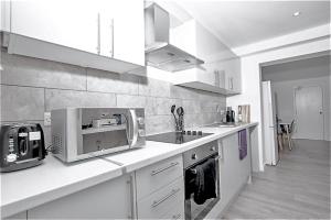 a white kitchen with a microwave and a sink at Dunamis Staycation 4 in Croydon +15 photos