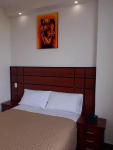 a bed with a wooden headboard with a picture above it at HOTEL DEL RIVER MONUMENTO in Sangolquí