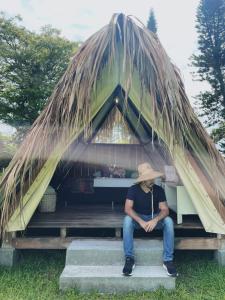 un hombre sentado en un banco en una cabaña con techo de paja en Terra Glamping, en San Pedro