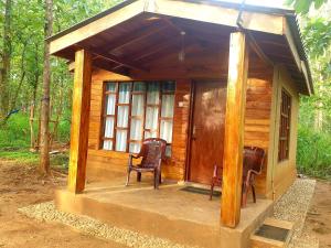 Cabaña de madera pequeña con porche con 2 sillas en Mini Jungle Canopy Udawalawe, en Udawalawe