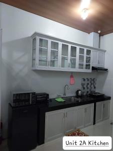 a kitchen with white cabinets and a black counter top at FLB Apartelle Los Banos in Los Baños
