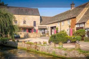 a large stone building next to a river at Charming Cottage in Heart of Bourton-on-the Water in Bourton on the Water