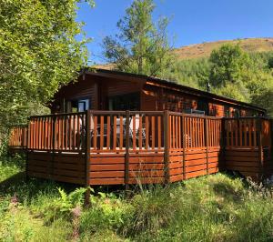 a cabin in the woods with a large deck at Balquhidder Braes Holiday Park in Lochearnhead
