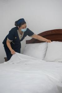 a woman in a mask is making a bed at Hotel Exelsior in Cúcuta