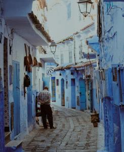 a man walking down an alley with blue buildings at Hotel Ouarzazate in Chefchaouen
