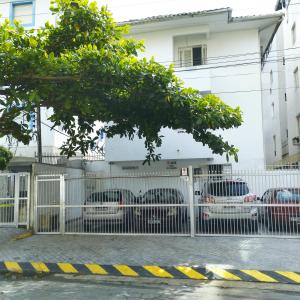 une clôture blanche avec des voitures garées devant un bâtiment dans l'établissement PRAIA ENSEADA - WI-FI e AR CONDICIONADO, à Guarujá