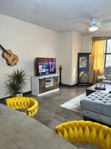 Luxury Midtown Flats near Downtown Memphis & FedEx Forum في ممفيس: غرفة معيشة مع كراسي صفراء وتلفزيون بشاشة مسطحة