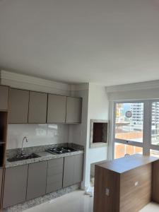 a kitchen with white cabinets and a large window at Recanto Meia Praia in Itapema