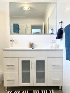 a white bathroom with a sink and a mirror at Bermagui Beach Apartment in Bermagui
