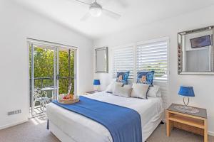 a white bedroom with a bed and windows at Verano Resort Noosa in Noosaville