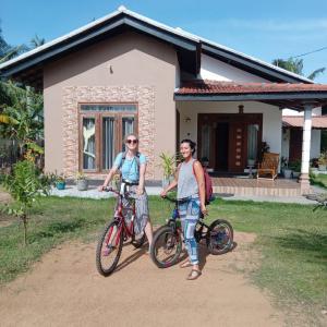 duas pessoas em frente a uma casa com as suas bicicletas em Aiden Homestay em Pasikuda