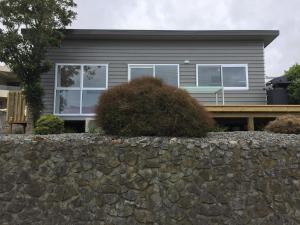 a house with a stone wall in front of it at Horizon View in Waihi Beach