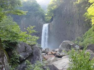 a waterfall in a forest next to rocks and trees at 池の平温泉 ロッジ コクハ in Myoko