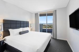 a bedroom with a large white bed and a flat screen tv at Meriton Suites Broadbeach in Gold Coast
