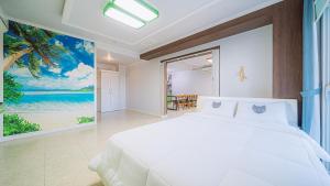 Un dormitorio con una cama blanca y una pintura del océano en Geojerowa Pension, en Geoje