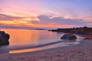 a sunset on a beach with rocks in the water at Appartamento Ognina Siracusa in Ognina