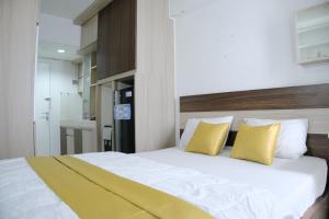 - une chambre avec un grand lit blanc et des oreillers jaunes dans l'établissement Kia Servised Apartmen at Grand Sentraland Karawang, à Karawang