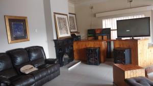a living room with a black leather couch and a television at Jay's Guest House in eMalahleni