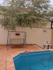 a swimming pool in front of a white wall with a tree at Villa Marmara in Al Madinah