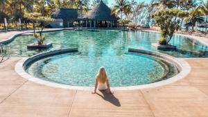 a woman sitting in front of a swimming pool at Outrigger Mauritius Beach Resort in Bel Ombre