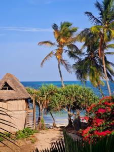 a beach with palm trees and a hut and the ocean at Ladha ya Zanzibar Boutique Guesthouse in Jambiani