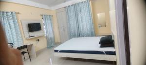 a bedroom with a bed with blue curtains and a tv at GRUHAM SOJOURN HOMESTAY in Guwahati