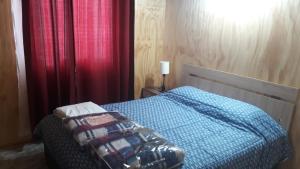 1 dormitorio con cama con edredón azul y cortinas rojas en Cabañas Claire, en El Quisco