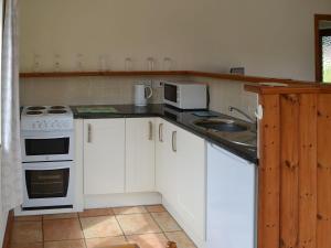 a kitchen with white cabinets and a stove and a sink at The Conifers in Hevingham