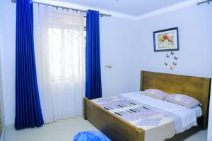 1 dormitorio con 1 cama con cortinas azules y ventana en Karibu Namugongo, en Kampala