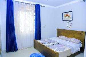 a bedroom with a bed with blue curtains and a window at Karibu Namugongo in Kampala