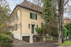 a yellow house with green shutters and a tree at Centrally located House with garden in Zurich