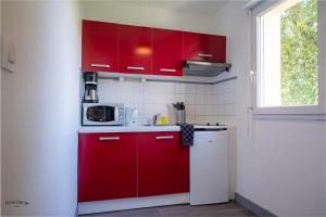 uma cozinha com armários vermelhos e um micro-ondas em Apparthôtel Mont Saint Michel - Résidence Fleurdumont em Beauvoir