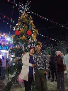 Ein Mann und eine Frau stehen vor einem Weihnachtsbaum in der Unterkunft Hotel Sweetland in Sauraha