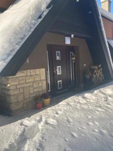 una casa con una puerta negra en la nieve en Penzion Karolinka en Karolinka