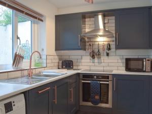cocina con armarios azules, fregadero y microondas en Castle Street Cottage en Narberth