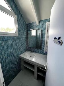 a blue tiled bathroom with a sink and a window at Bungalow Sucrier, les pieds dans l'eau in Terre-de-Haut