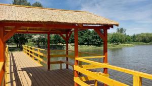 a wooden boardwalk with a thatch roof and the water at Gólya-Tó Vendegház 2 in Vajdácska
