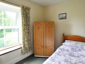 a bedroom with a bed and a wooden cabinet and a window at Ashberry Cottage in Rievaulx