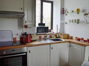 cocina con armarios blancos, fregadero y microondas en Honeysuckle Cottage, en Nerquis
